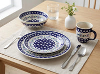 A place setting on a light wood table featuring a matching ceramic dinnerware set with a deep blue and white floral pattern, including a plate, bowl, mug, and cutlery on a beige placemat.