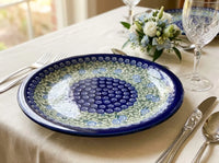 Polish Pottery Plate in Seaside Swirl pattern on a linen tablecloth with silverware, crystal glasses, and a vase of flowers