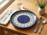 Polish pottery plate in Alyce pattern with silverware and a potted plant on a wood table.