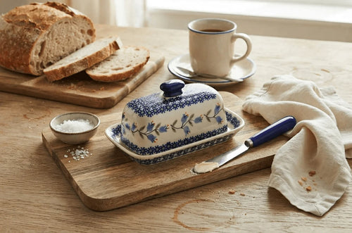 Polish pottery tulip butter dish on wood cutting board with knife, bread, and butter.