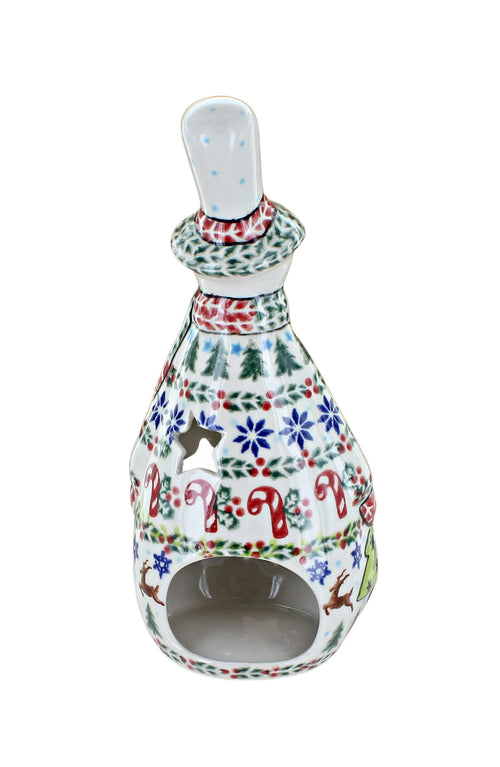 A ceramic Christmas candle holder with a white base decorated with colorful hand-painted holiday motifs including pine trees, snowflakes, candy canes, and reindeer, featuring a cutout front and a small top opening.
