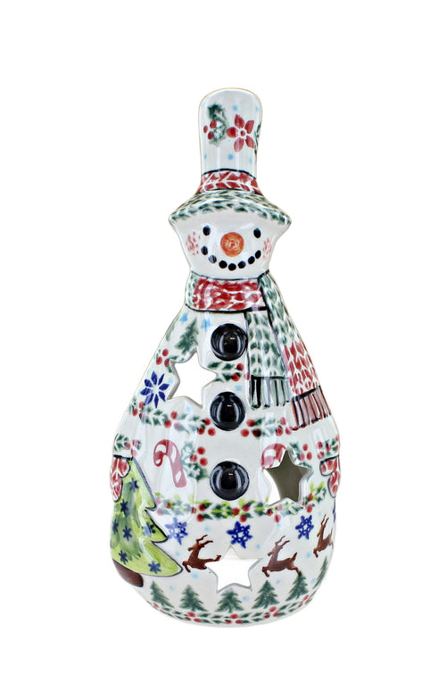 A ceramic snowman-shaped candle holder with a white base decorated with colorful Christmas patterns including red flowers, green holly, blue snowflakes, brown reindeer, and a red-and-white striped scarf. The front has three black button details, and the top and sides have star-shaped cutouts.