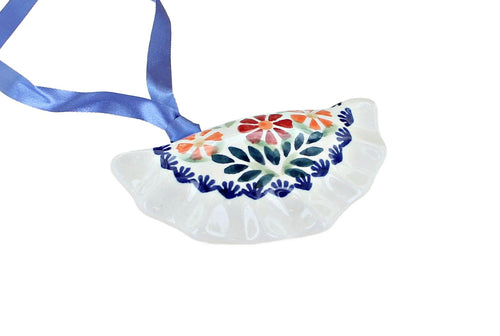A white ceramic Polish Christmas ornament shaped like a dumpling, decorated with colorful floral patterns in orange, red, and green, finished with a blue scalloped border and a blue ribbon hanger.