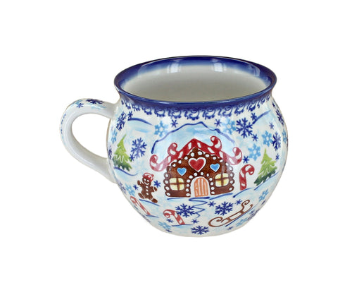 A ceramic mug decorated with a winter holiday scene featuring a gingerbread house, candy canes, snowflakes, and a sleigh on a white background.