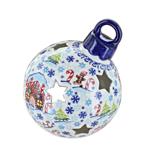 A ceramic Christmas ornament shaped like a sphere with a hanging loop at the top. The ornament is decorated with a light blue and white winter pattern featuring snowflakes, candy canes, gingerbread men, Christmas trees, and a gingerbread house, with star-shaped cutouts.