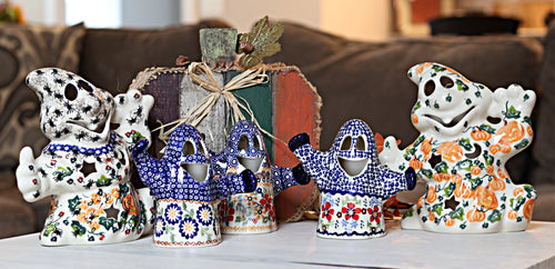 A set of five hand-painted ceramic ghost figurines decorated with colorful floral and geometric patterns, arranged on a white tablecloth in front of a rustic wooden box on a couch.