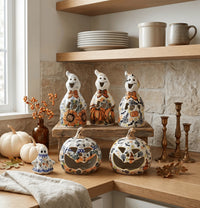 A set of ceramic Halloween decorations displayed on a wooden kitchen counter, including three ghost figurines and two carved jack-o'-lanterns, decorated with a colorful floral pattern.