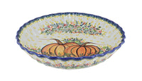 A ceramic pie plate with a scalloped rim, decorated with a hand-painted design featuring orange pumpkins, yellow dots, and floral patterns on a white background.