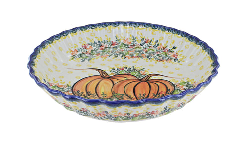 A ceramic pie plate with a scalloped rim, decorated with a hand-painted design featuring orange pumpkins, yellow dots, and floral patterns on a white background.
