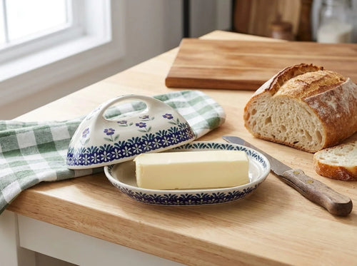 Polish pottery butter dish in Blue Daisy pattern resting on wood kitchen counter with rustic bread, butter, and linens.