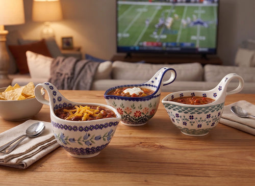 Three decorative ceramic soup servers with floral patterns are arranged on a wooden table in a cozy living room setting, with a TV and couch blurred in the background.