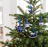 Blue and white ceramic Christmas tree ornaments hanging on a decorated Christmas tree, including a teapot, house, pumpkin, and teacup.