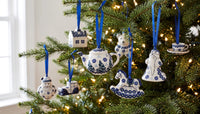 Blue and white ceramic Christmas tree ornaments hanging on a lit green Christmas tree, including a teapot, rocking horse, house, and Santa Claus figure.