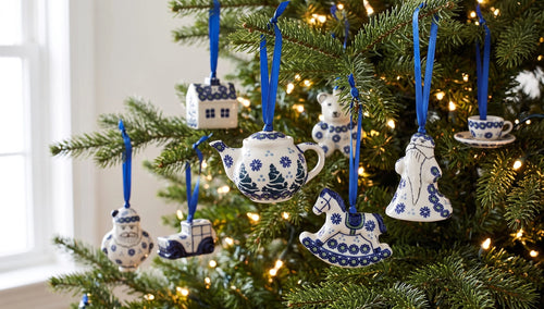 Blue and white ceramic Christmas tree ornaments hanging on a lit green Christmas tree, including a teapot, rocking horse, house, and Santa Claus figure.