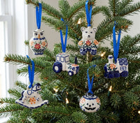 A set of six hand-painted ceramic Christmas tree ornaments in Polishware style, featuring an owl, bear, tractor, house, rocking horse, and pumpkin, hanging on a green Christmas tree with blue ribbons.