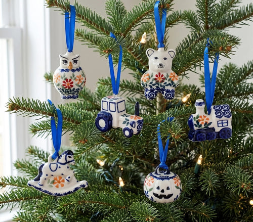 A set of six hand-painted ceramic Christmas tree ornaments in Polishware style, featuring an owl, bear, tractor, house, rocking horse, and pumpkin, hanging on a green Christmas tree with blue ribbons.