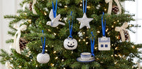 A set of ceramic Christmas tree ornaments with blue and white patterns, hanging on a decorated green Christmas tree with lights.