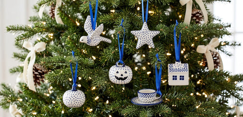 A set of ceramic Christmas tree ornaments with blue and white patterns, hanging on a decorated green Christmas tree with lights.