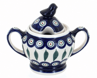 A ceramic sugar bowl with a matching lid featuring a bird topper, decorated with a traditional Polish pattern of blue, white, green, and red concentric circles and leaf motifs.