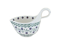 A white ceramic saucepan with a loop handle, decorated with blue and green floral and geometric patterns, shown on a plain white background.