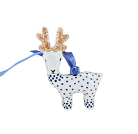 A ceramic Christmas ornament shaped like a white deer with blue polka dots, brown antlers with white dots, and a blue ribbon hanger, shown on a plain white background.