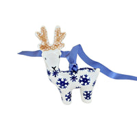 A ceramic reindeer ornament with blue snowflakes on a white body, featuring tan antlers and a blue ribbon hanger, shown against a plain white background.