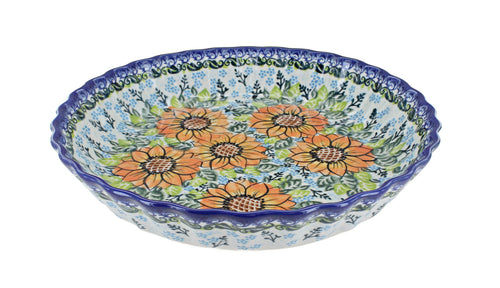 A hand-painted ceramic pie plate with a scalloped rim, featuring a floral pattern of orange sunflowers, blue blossoms, and green leaves on a white background with a blue border.