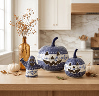 Three ceramic jack-o'-lantern pumpkins and a ghost-shaped container in a blue and white speckled pattern, styled on a wooden kitchen counter with small pumpkins, a vase of dried stems, and autumn leaves.
