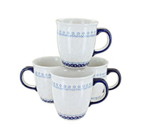 Four white ceramic mugs with dark blue handles and rims, decorated with a blue geometric pattern band near the top and bottom, arranged on a white background.